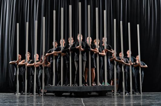 People in black standing on a stage holding tall metal bars vertically
