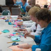 A group of people sit at a table doing arts and crafts.