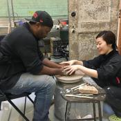 A pottery student is assisted in shaping their clay by their professor.