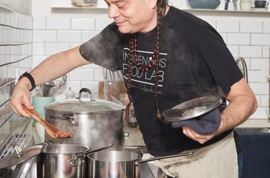 A person stands over a stove with many pots on it, cooking a variety of foods.