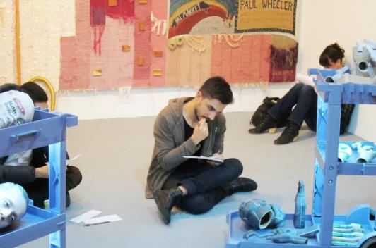 Three people sit in a room covered in art, writing in notebooks.