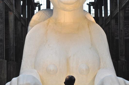 A small child stands in front of a large white statue of a woman sphinx.