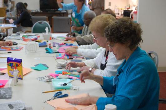 A group of people sit at a table doing arts and crafts.
