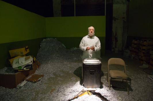 A man in a room with a shredder, surrounded by shredded paper