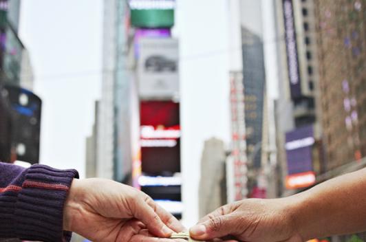 Times Square is the background as one hand passes a key to another hand.