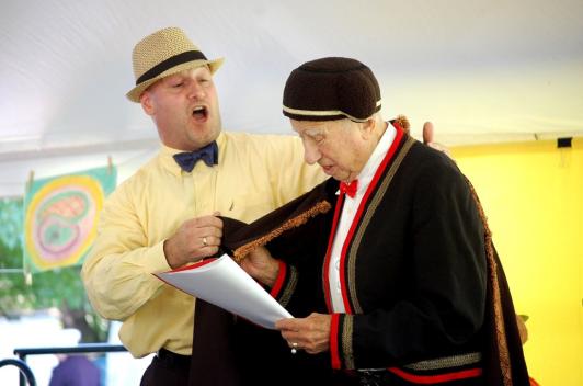 Two people in costumes stand on a stage in a community room singing.
