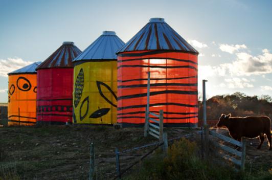 At a farm, four cylinder towers use light fabric as the walls. The sun shines through the fabric.