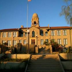 The sunsets on a light brown building that features two floors with windows and a tower in the middle.