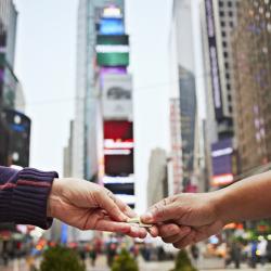 Times Square is the background as one hand passes a key to another hand.