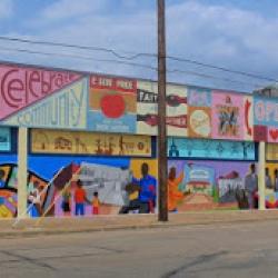 A low building along a street is covered in murals featuring images like reading a book or people playing as well as words like read, and community.