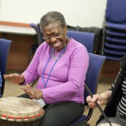 Three people sitting in a circle drumming on different sized drums.