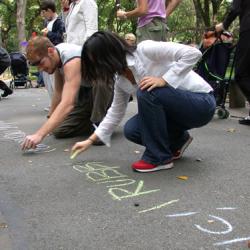 Two people lean over to write words in chalk on the pavement.