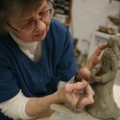 A person works on a clay sculpture, carving intricate features into it.