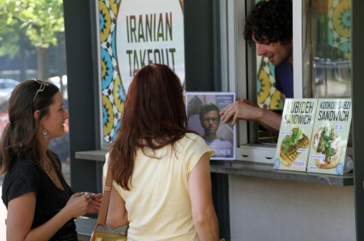 Two people standing at an ordering window, talking to the person inside.