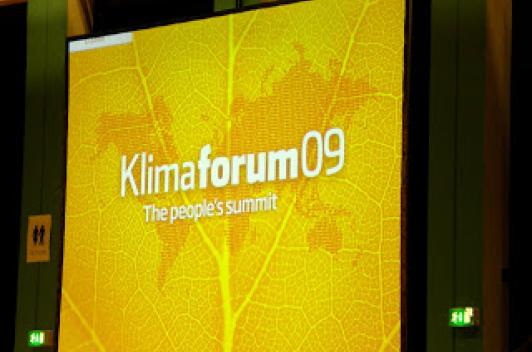 Yellow powerpoint slide with a slightly darker yellow imprint of the world map. The slide features the words Klimaforum09.