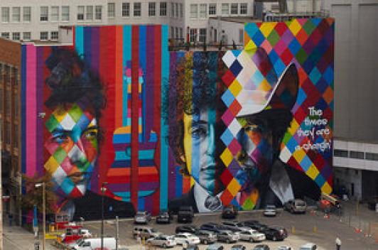 Building with a mural painted on it. The mural features stripes and squares of various colors and the faces of people