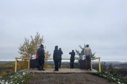 On a hill there is an overlook built. A few people stand looking over it.