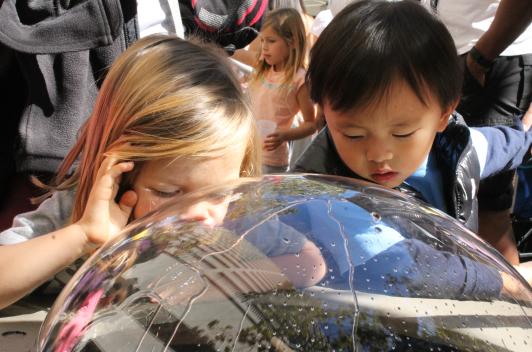 Two children peering into a plastic bubble over a water feature