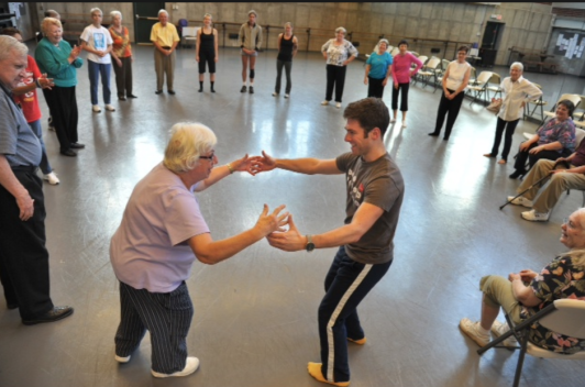 Two people dancing together in a circle of people in a large recreation room.