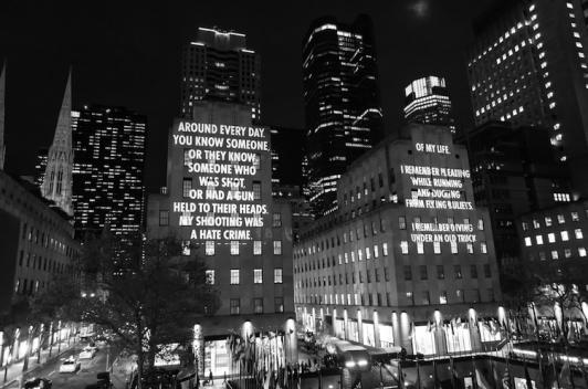 A black and white photo of buildings in a city with text with gun violence facts projected on them.