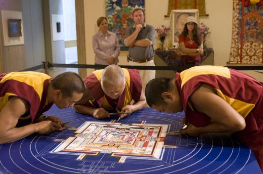 Three monks bending over a table working on creating a mandala