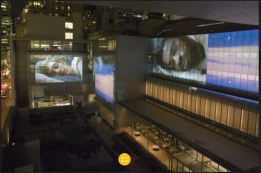 Two glass buildings are lit up in the night with images of people sleeping.