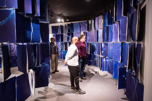 Three people stand in the midst of strings of blue panels. 