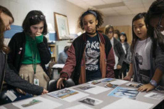 A group of young people stand around a table looking at printed out photos.