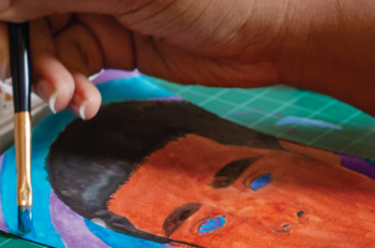 A hand holds a brush, painting a colorful image of another person.