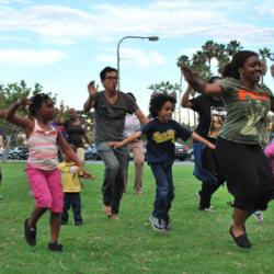 A group of adults and children dance on a green lawn.