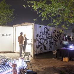 Two people looking into a shipping container turned into an art exhibit labeled Kids Stuff