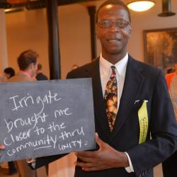 A person holding a chalkboard with the written message "Irrigate brought me closer to the community through unity"
