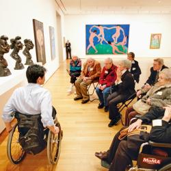 Photo of a person in a wheel chair guiding others through an art exhibit