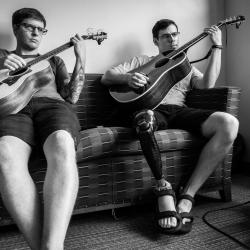 Two people on the couch playing guitar. The photo is in black and white.