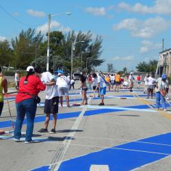 People at an outdoor court repainting it with different colored stripes of blue