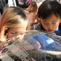 Two children peering into a plastic bubble over a water feature
