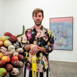 A person in a colorful shirt stands in front of a sculpture of various fruits.
