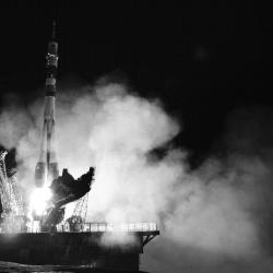 A black and white photo of a rocket launching, with smoke surrounding the bottom of the rocket.