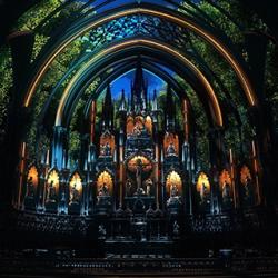Inside of a basilica. The bottom is lit with candles and the top is lit with trees and a dark sky