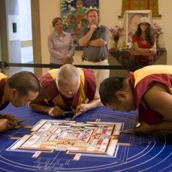 Three monks bending over a table working on creating a mandala
