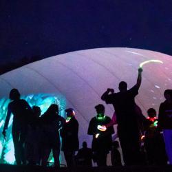 Silhouettes of people at night against a large white dome that has various images projected on it.