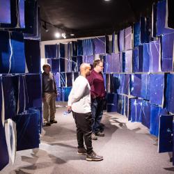 Three people stand in the midst of strings of blue panels. 