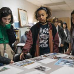 A group of young people stand around a table looking at printed out photos.