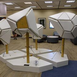 A sculpture with four separate pieces. All are white, padded shapes. The sculpture is in a computer room.