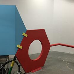 A blue and red sculpture featuring two hexagons connected together and three long red poles connected to the red hexagon.