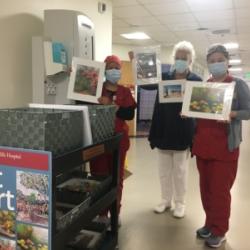 Employees holding artwork towards the camera with the art cart in the lower left corner on display