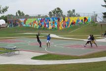 Some young adults playing basketball on a court in front of a colorful mural