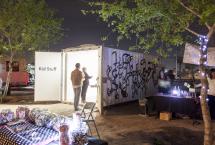 Two people looking into a shipping container turned into an art exhibit labeled Kids Stuff