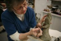 A person works on a clay sculpture, carving intricate features into it.