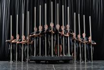 People in black standing on a stage holding tall metal bars vertically